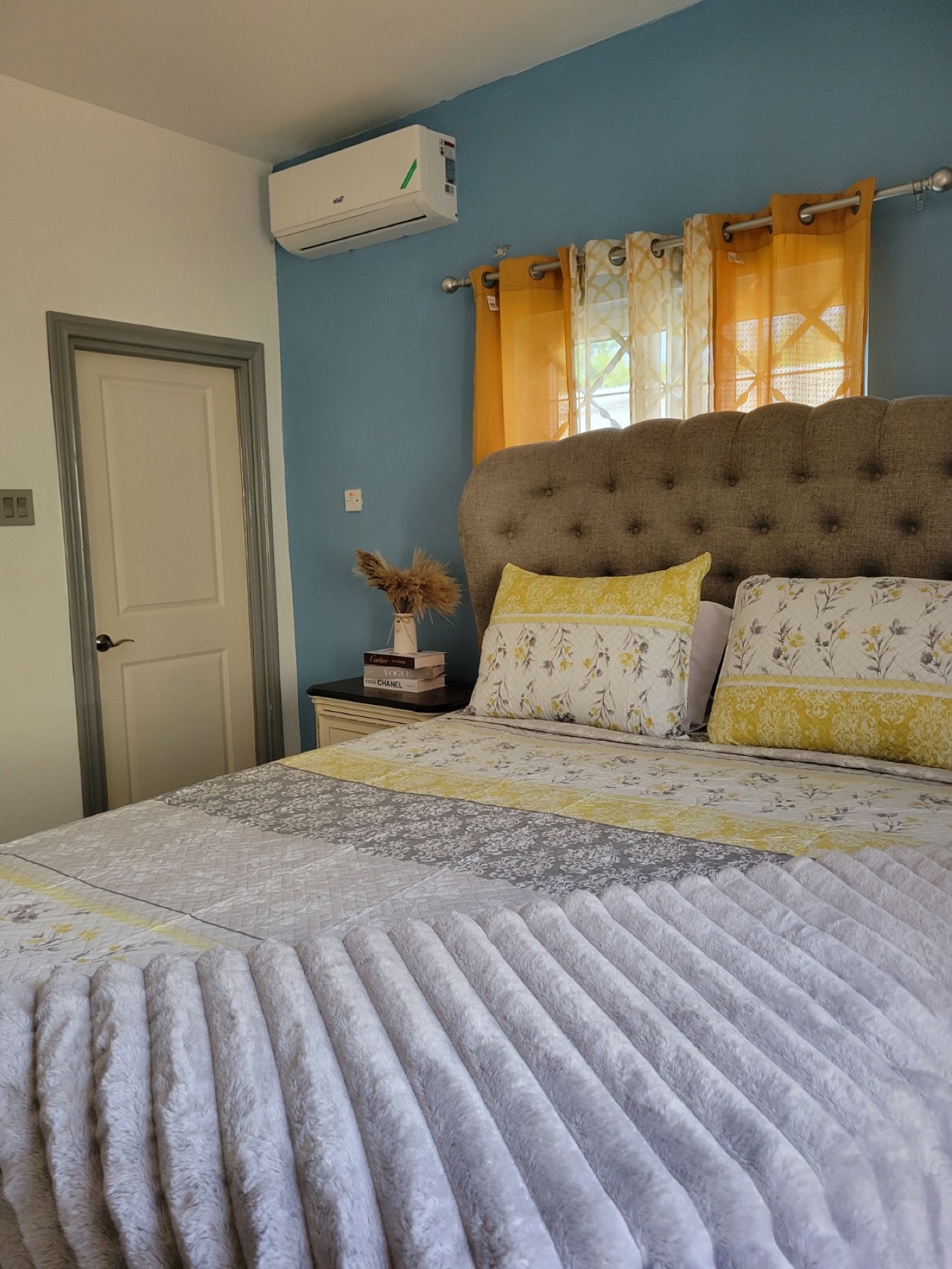 An en-suite bedroom with a teal feature wall, a padded headboard and gold curtains