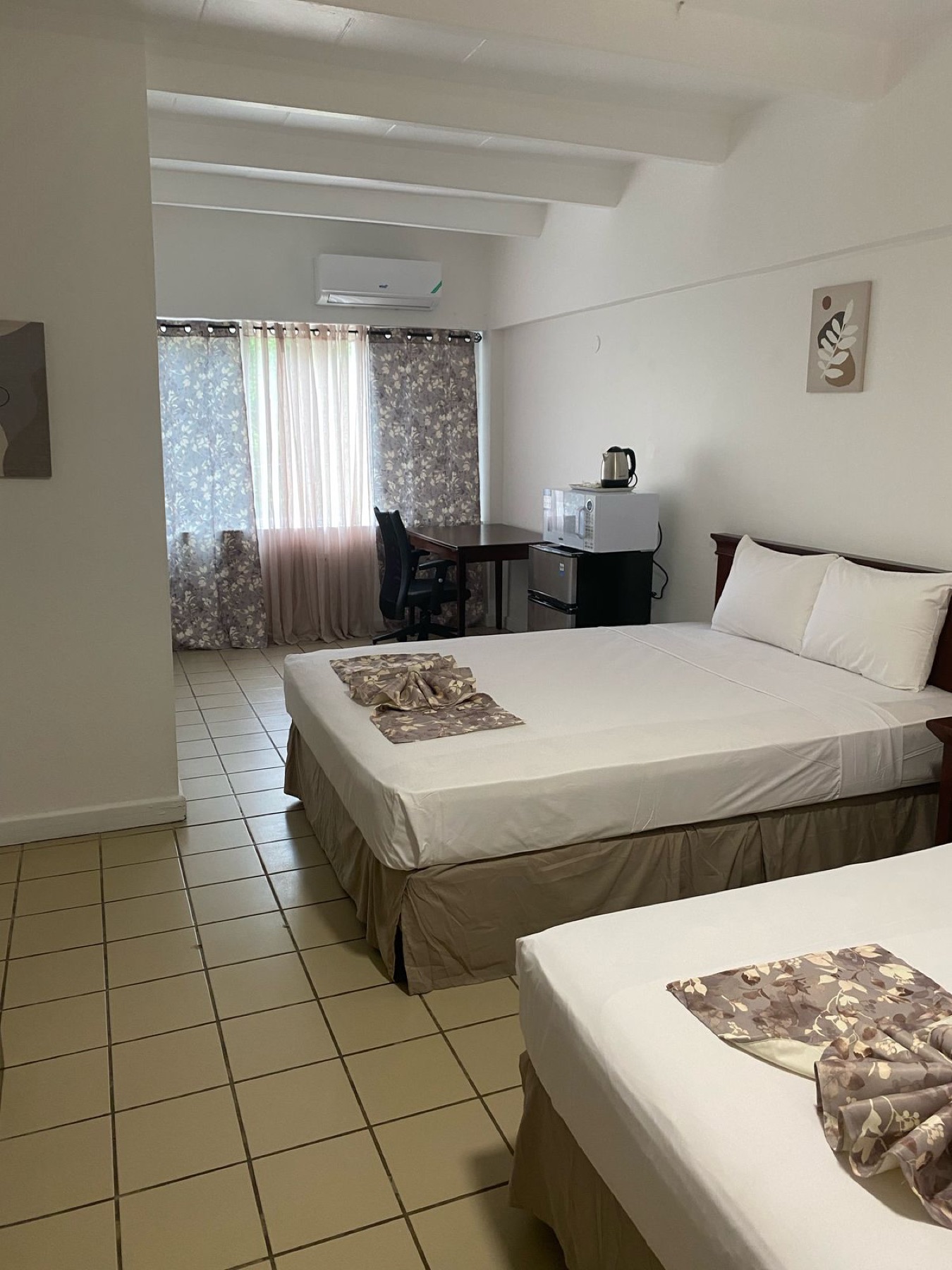 A suite with two beds, an air conditioner and a table by the window