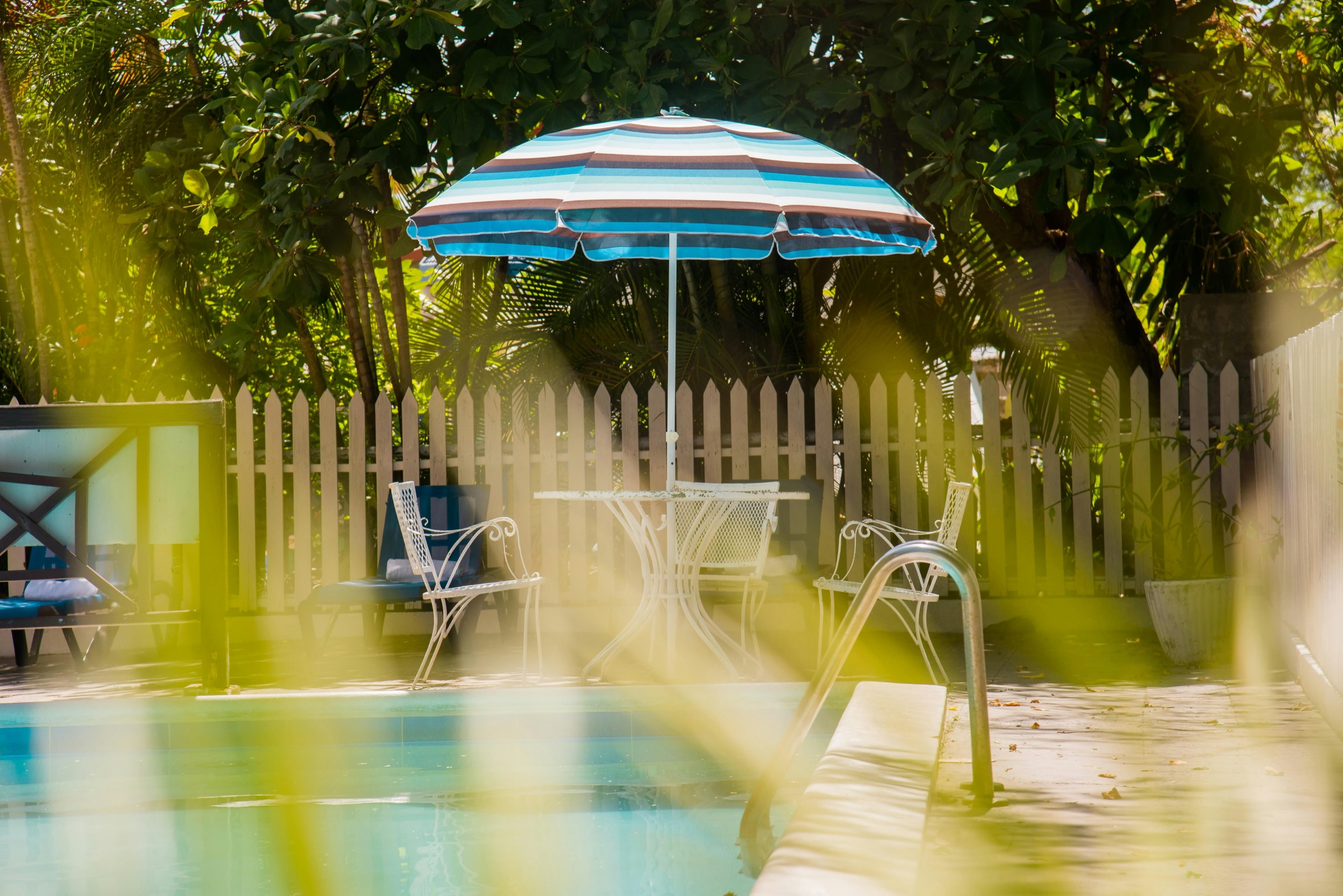 The pool at Pineapple Court in golden afternoon light, a striped umbrella and garden chairs behind palm fronds