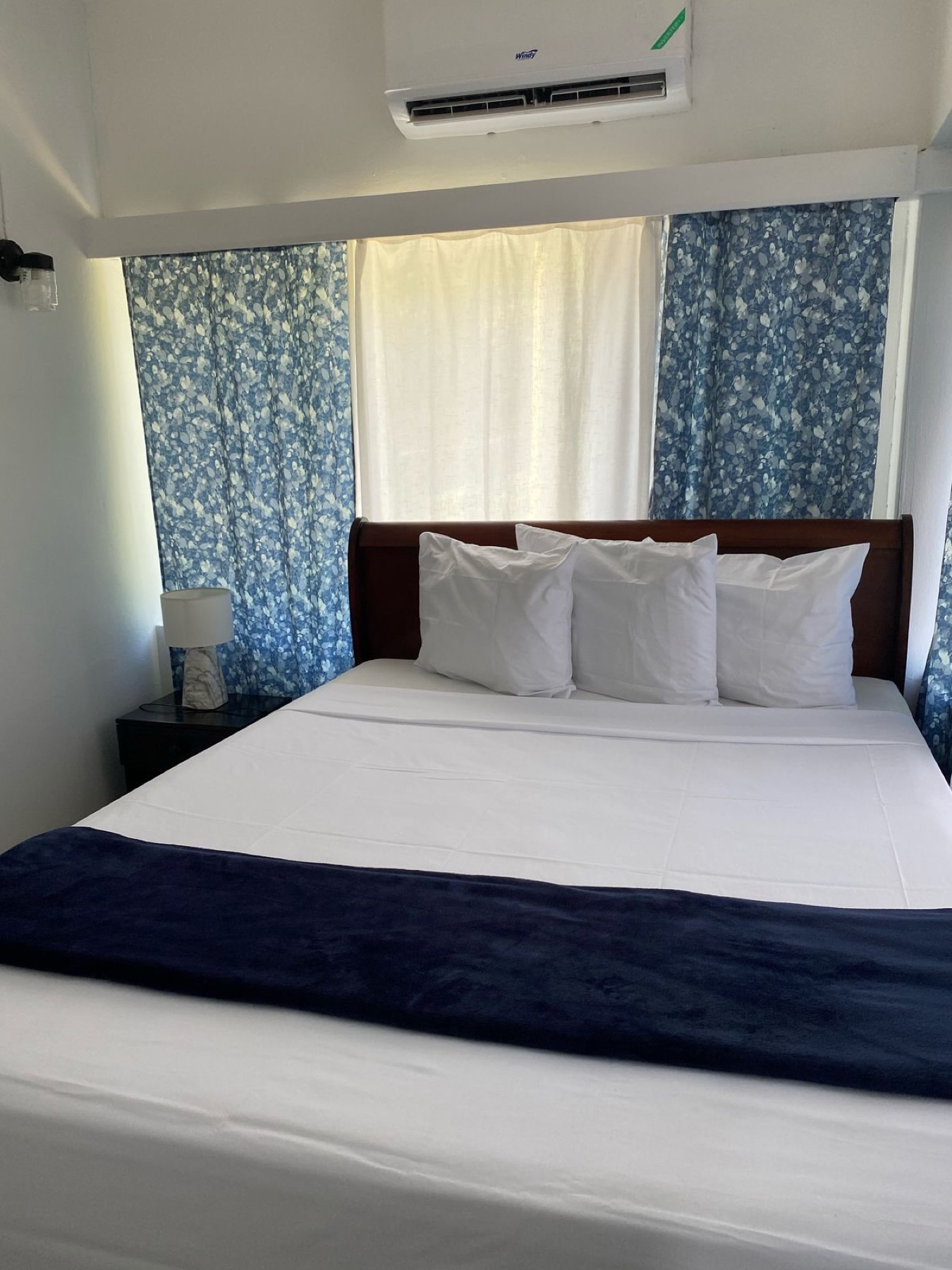 A made-up bed with white linens and a navy throw, blue floral curtains behind